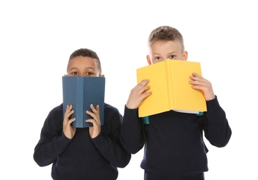 Portrait of cute children in school uniform hiding behind books on white background