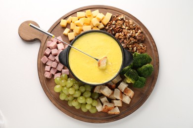 Photo of Fondue with tasty melted cheese, fork and different products on white table, top view