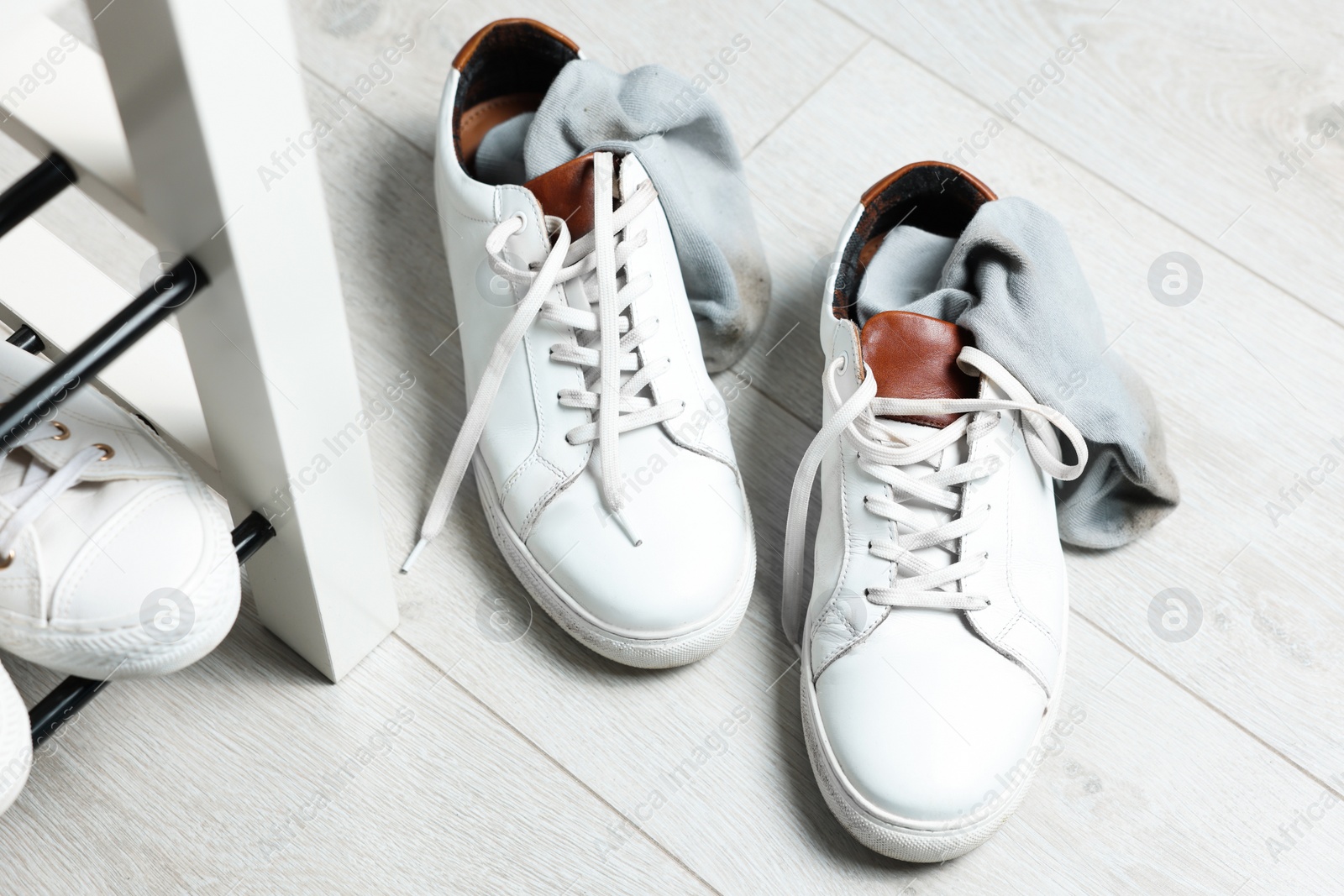 Photo of Sneakers with dirty socks on white wooden floor indoors