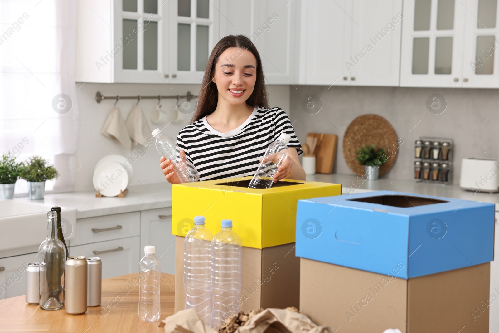 Photo of Smiling woman separating garbage at table in kitchen