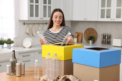 Photo of Smiling woman separating garbage at table in kitchen