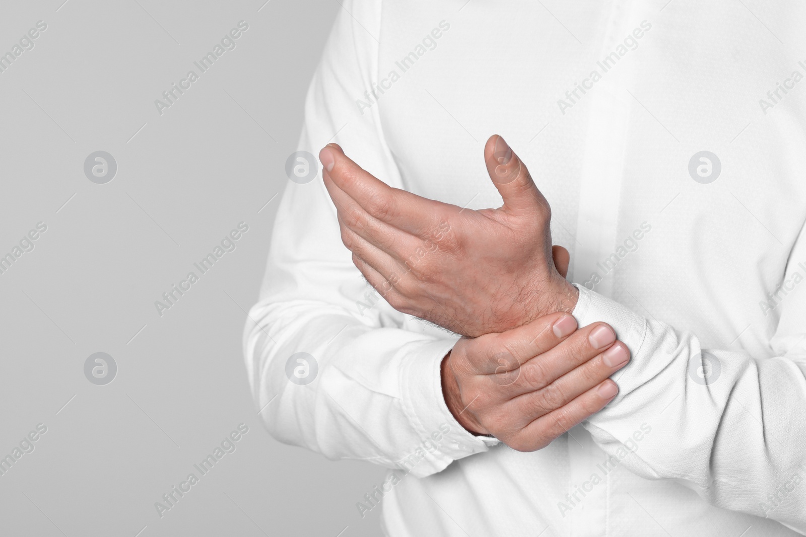 Photo of Man suffering from pain in his hand on light background, closeup view with space for text. Arthritis symptoms