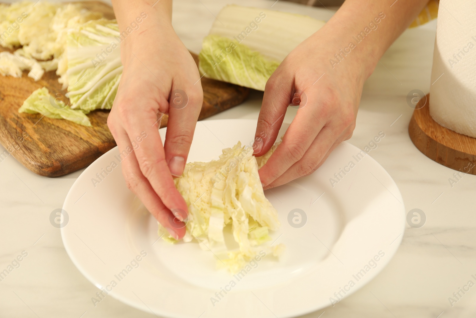 Photo of Woman putting cut Chinese cabbage into plate at white kitchen table, closeup