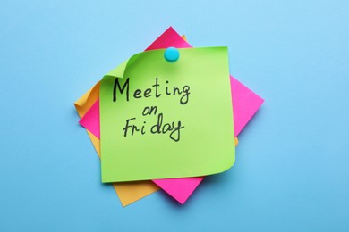 Photo of Paper note with words Meeting on Friday pinned to light blue background