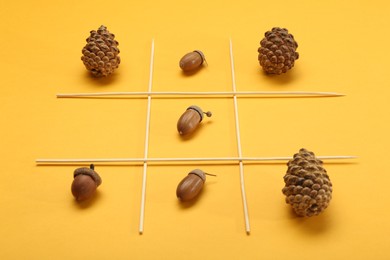 Tic tac toe game made with acorns and pine cones on yellow background