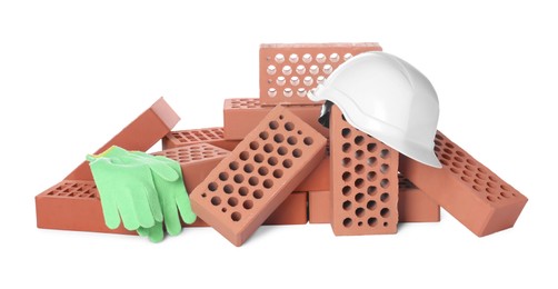 Photo of Pile of red bricks, hard hat and gloves on white background