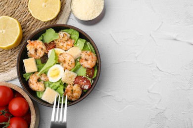Delicious Caesar salad with shrimps and fork served on white textured table, flat lay. Space for text