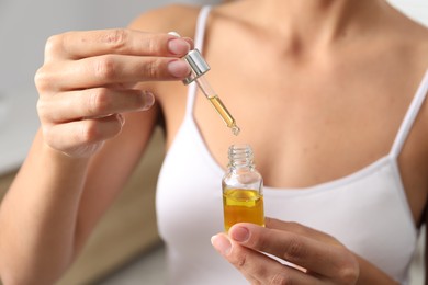 Photo of Woman with bottle of cosmetic serum on blurred background, closeup