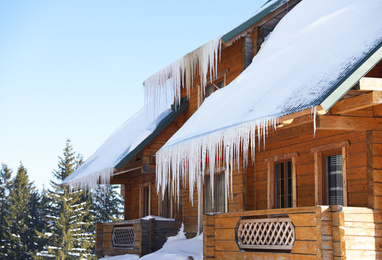 Modern wooden cottage with icicles on sunny day. Winter vacation