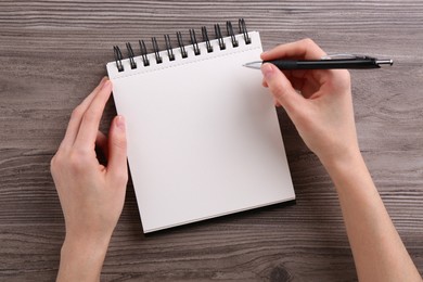 Photo of Woman writing in notebook at wooden table, top view