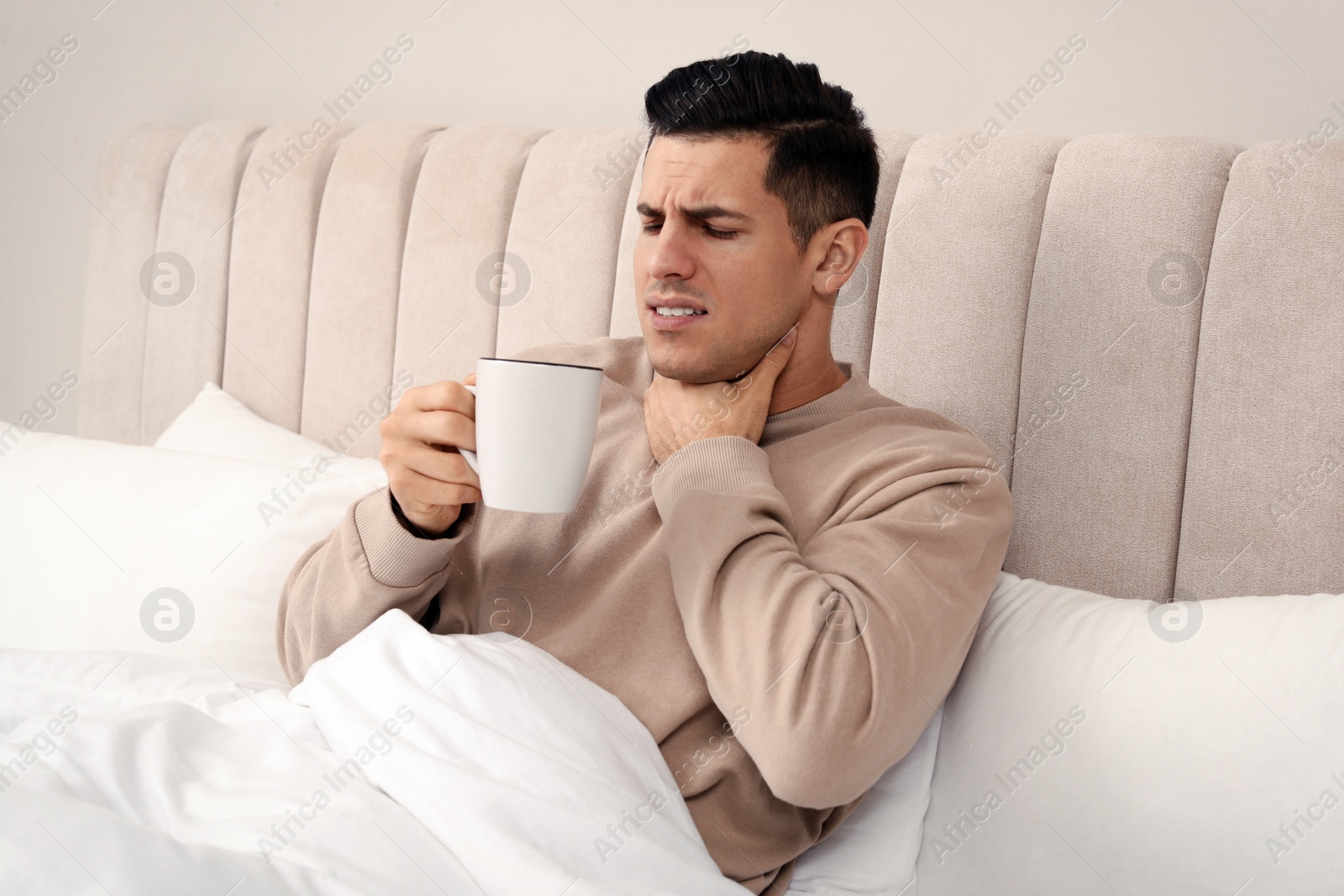 Photo of Sick man with cup of hot drink in bed at home