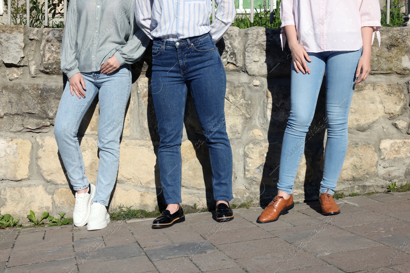 Photo of Women in stylish jeans near stone wall outdoors on sunny day, closeup