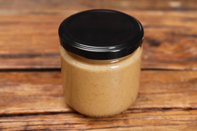 Tasty nut paste in jar on wooden table, closeup