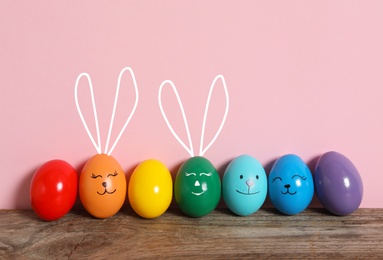 Image of Two eggs with drawn faces and ears as Easter bunnies among others on wooden table against pink background
