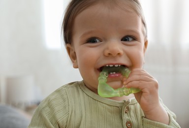 Photo of Cute baby girl with teething toy at home, closeup