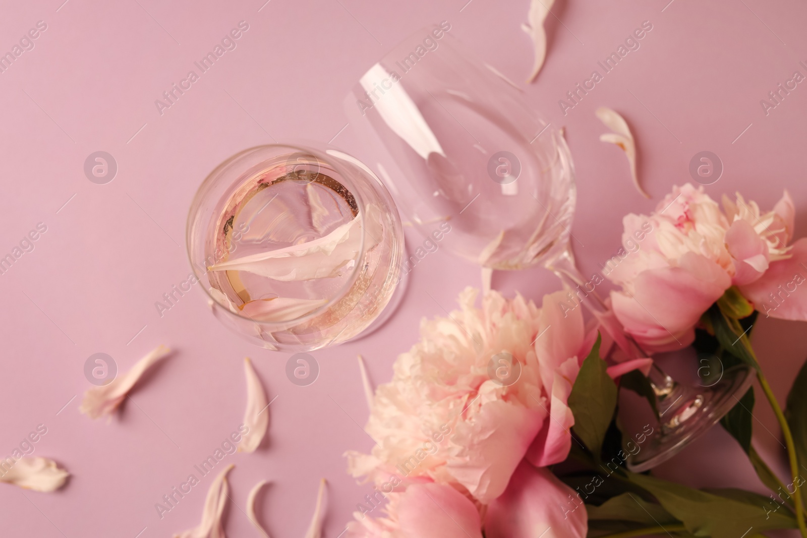 Photo of Glasses with rose wine and beautiful peonies on pink background, flat lay