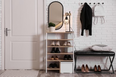 Photo of Shelving unit with shoes and different accessories near white brick wall in hall. Storage idea