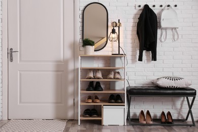 Shelving unit with shoes and different accessories near white brick wall in hall. Storage idea