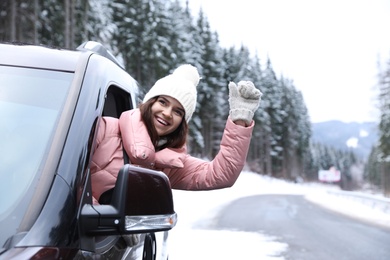 Young woman driving car and looking out of window on road. Winter vacation