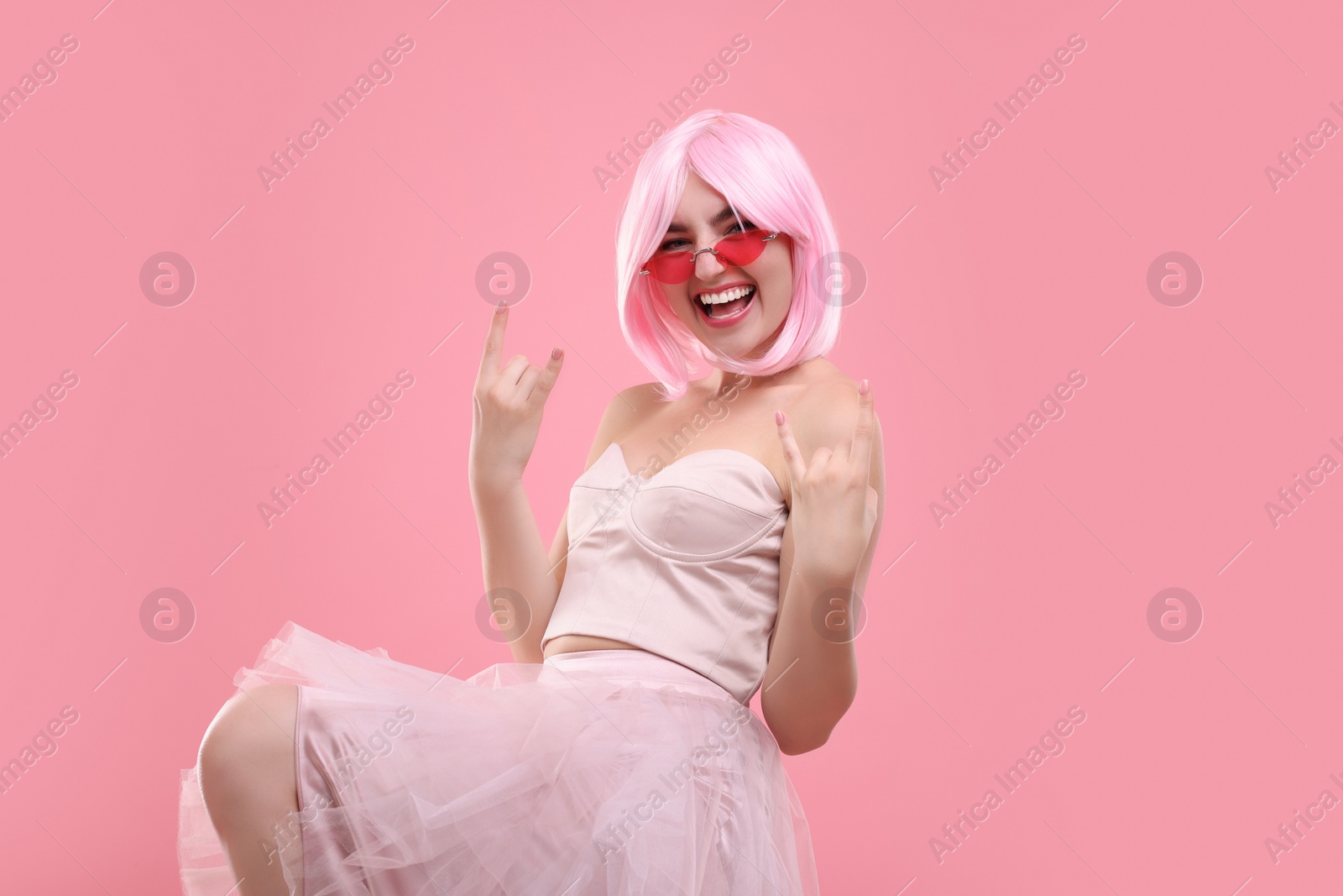 Photo of Pink look. Beautiful woman in wig and bright sunglasses showing rock sign on color background