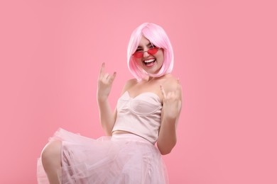 Photo of Pink look. Beautiful woman in wig and bright sunglasses showing rock sign on color background