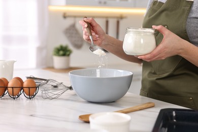 Housewife adding flour into bowl at white marble table in kitchen, closeup. Cooking process