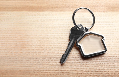 Key with trinket in shape of house on wooden background. Real estate agent services