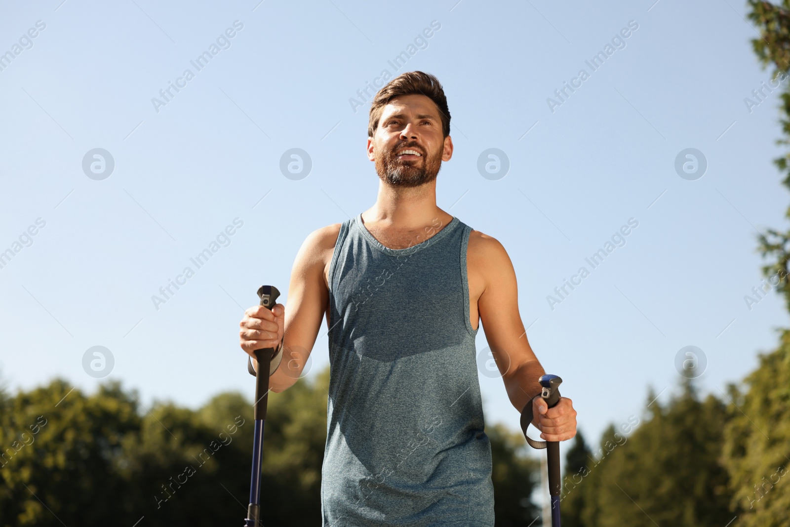 Photo of Man practicing Nordic walking with poles outdoors on sunny day