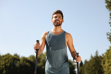 Photo of Man practicing Nordic walking with poles outdoors on sunny day