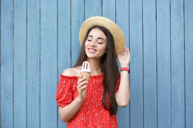 Happy young woman with delicious ice cream in waffle cone near wooden wall