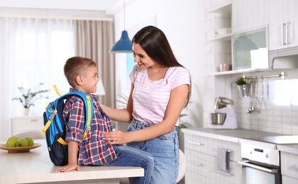 Photo of Happy mother and little child with backpack ready for school in kitchen