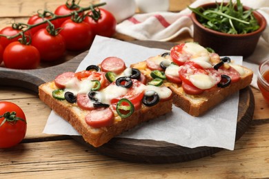Photo of Tasty pizza toasts, arugula and tomatoes on wooden table