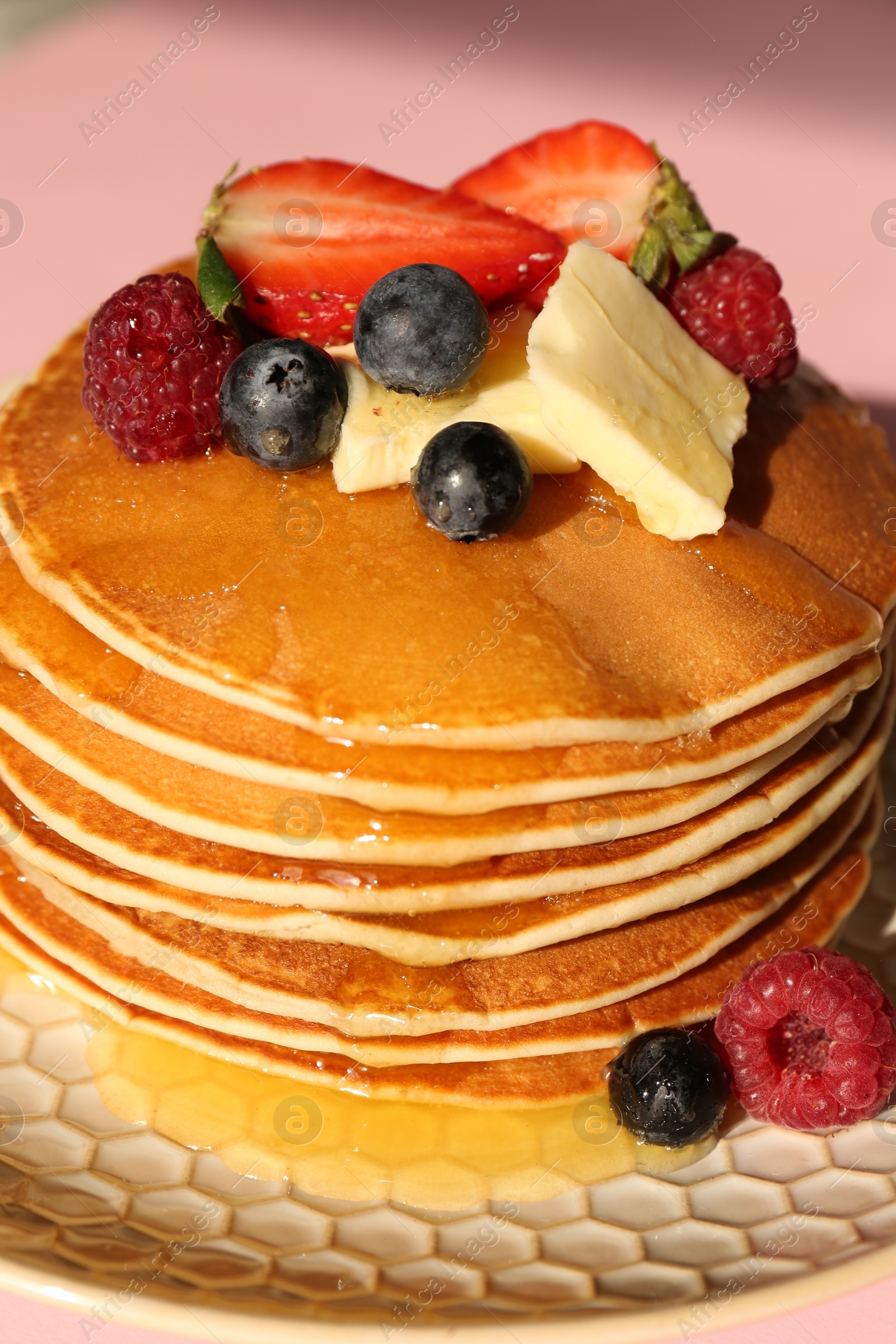 Photo of Delicious pancakes with fresh berries, butter and honey on pink background, closeup