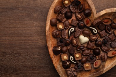 Photo of Heart shaped plate with delicious chocolate candies on wooden table, top view. Space for text