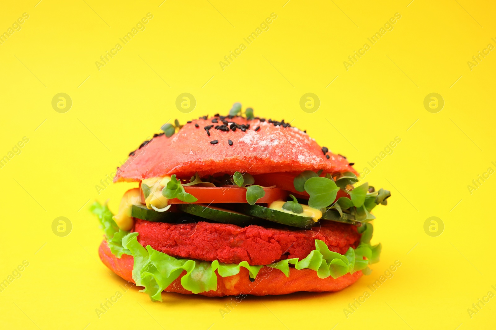 Photo of Tasty pink vegan burger with vegetables, patty and microgreens on yellow background, closeup