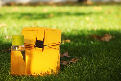 Photo of Lunch bag and bottle of water on green grass outdoors, space for text