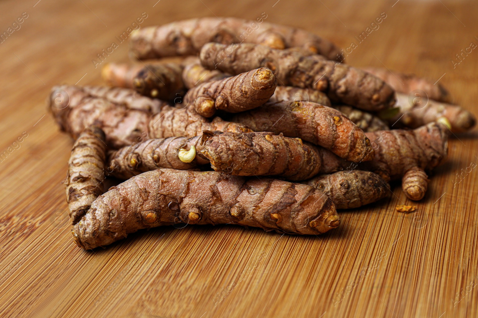 Photo of Many whole turmeric roots on wooden table