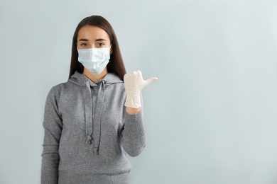 Photo of Woman in protective face mask and medical gloves pointing at something on grey background. Space for text
