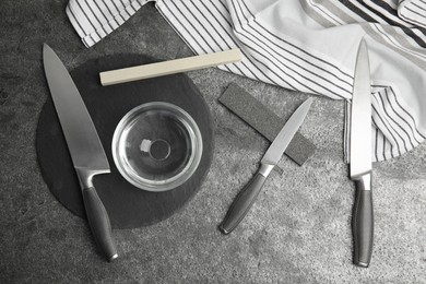 Photo of Sharpening stones, knives and water on grey table, flat lay
