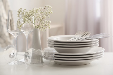 Set with clean dishes and vase of flowers on white table