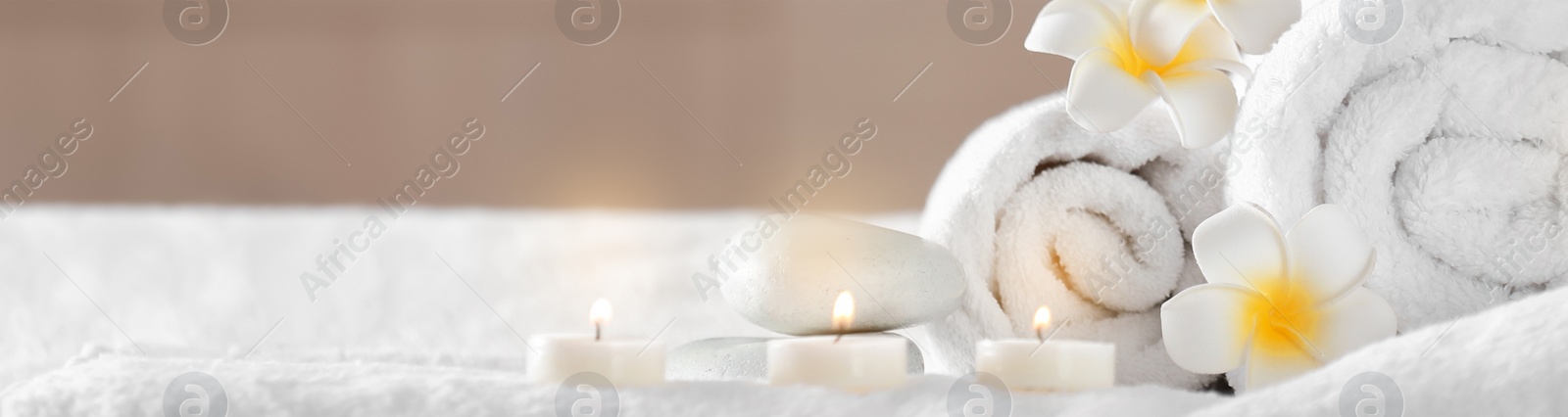 Image of Candles, hot stones, towels and plumeria flowers on massage table in spa cabinet, closeup. Banner design with space for text