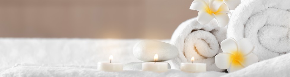 Image of Candles, hot stones, towels and plumeria flowers on massage table in spa cabinet, closeup. Banner design with space for text