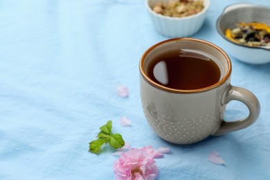 Photo of Cup of hot freshly brewed tea on light blue fabric, space for text