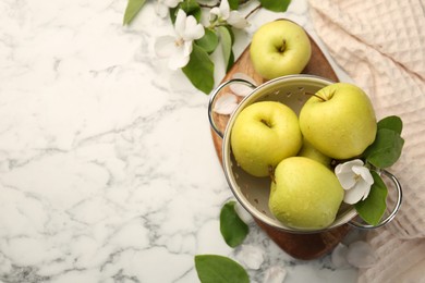 Photo of Colander with fresh apples and beautiful spring blossoms on white marble table, flat lay. Space for text