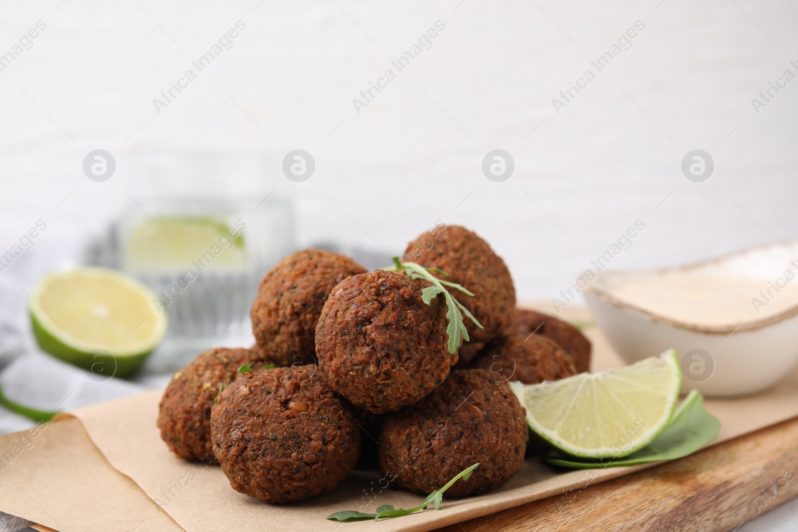 Photo of Delicious falafel balls, arugula, lime and sauce on table