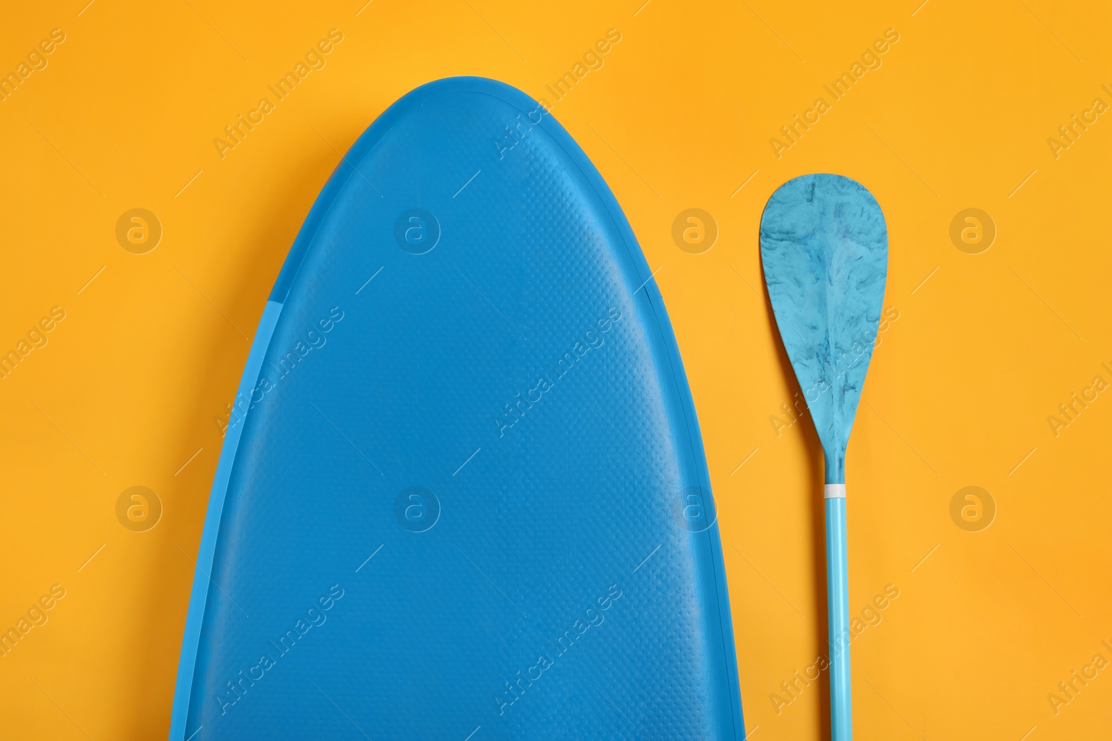 Photo of SUP board and paddle on yellow background, flat lay. Water sport