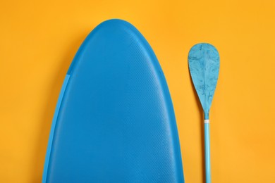 Photo of SUP board and paddle on yellow background, flat lay. Water sport