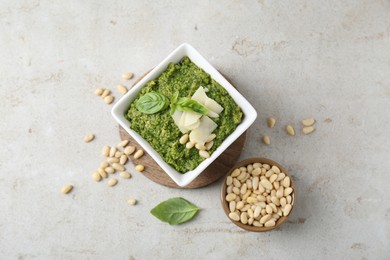 Photo of Bowl with delicious pesto sauce, cheese, pine nuts and basil leaves on light table, flat lay