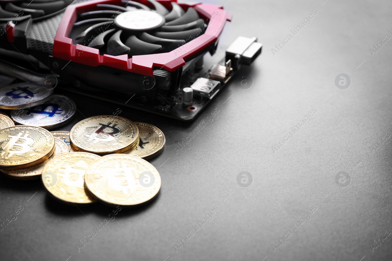 Photo of Modern video card and bitcoins on grey table, space for text