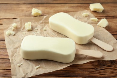 Photo of Glazed ice cream bars and white chocolate chunks on wooden table, closeup